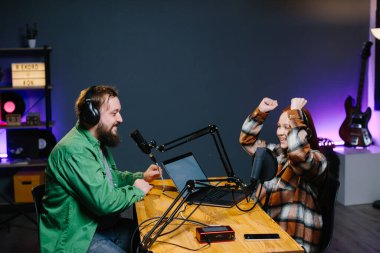 Bir podcast sunucusu ve bir konuk ev stüdyosunda canlı yayında sohbet ederken eğleniyorlar..