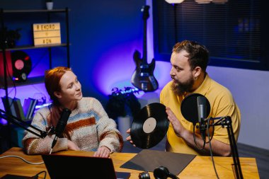 Bir radyo sunucusu stüdyoda bir konukla konuşur. Elinde plak plağı olan bir erkek blogcu bir kadınla canlı bir konuşma yapıyor..