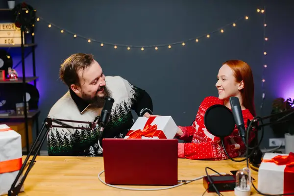 クリスマスストリームやビデオブログ 休日の服の陽気なプレゼンターは 加入者のための贈り物をラッフルします ホームスタジオでの新年の衣装で男性と女性のブロガー — ストック写真