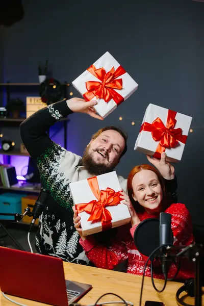 クリスマスストリームやビデオブログ 休日の服の陽気なプレゼンターは 加入者のための贈り物をラッフルします ホームスタジオでの新年の衣装で男性と女性のブロガー — ストック写真