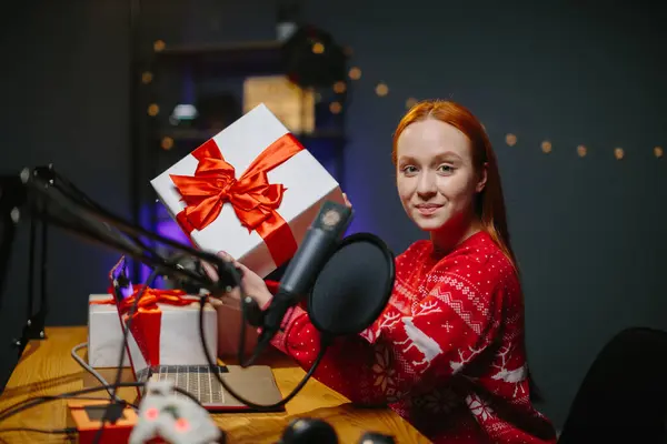 女の子のブロガーがチャンネルでクリスマスプレゼントをしている 家のスタジオで彼女の手で贈り物をクリスマスのセーターで女の子の肖像画 — ストック写真