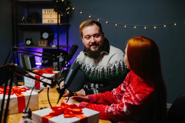 数人のブロガーがチャンネルでクリスマスプレゼントをしています クリスマスセーターのラジオプレゼンターは リスナーの間で贈り物のラッフルを行います — ストック写真