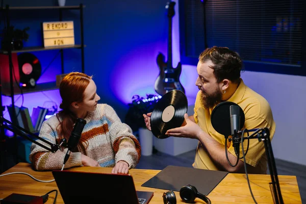 A radio presenter talks to a guest in the studio. A male blogger with a vinyl record in his hands is having a live conversation with a woman.