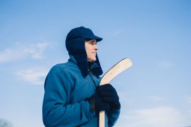 Gökyüzünün arka planında hokey sopasıyla yaşlı bir adamın portresi.