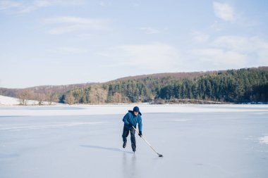 Yaşlı bir adam kışın donmuş bir gölde buz hokeyi yapıyor..