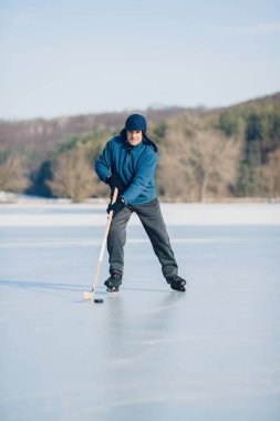 Yaşlı bir adam kışın donmuş bir gölde buz hokeyi yapıyor..