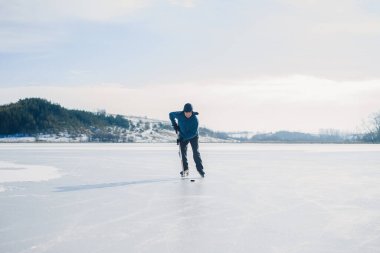 Yaşlı bir adam kış aylarında buz tutmuş bir gölde hokey sopalarıyla diski sıkıştırıyor..