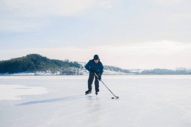 Yaşlı bir adam kış aylarında buz tutmuş bir gölde hokey sopalarıyla diski sıkıştırıyor..