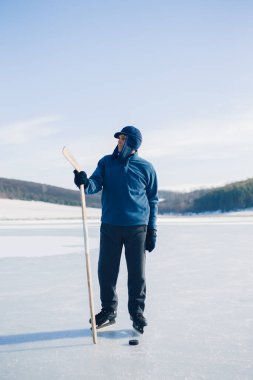 Yaşlı bir adam buz tutmuş bir gölde hokey sopasıyla diski sıkıştırma alıştırması yapıyor..