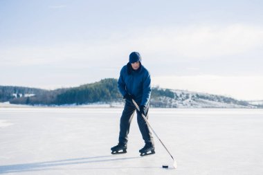 Yaşlı bir adam buz tutmuş bir gölde hokey sopasıyla diski sıkıştırma alıştırması yapıyor..