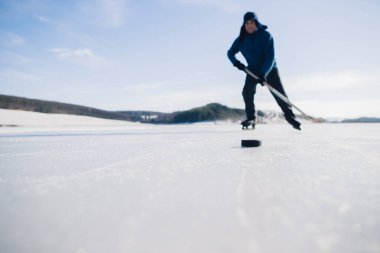 Yaşlı bir adam buz tutmuş bir gölde hokey sopasıyla diski sıkıştırma alıştırması yapıyor..