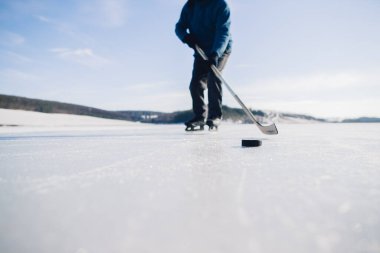 Yaşlı bir adam buz tutmuş bir gölde hokey sopasıyla diski sıkıştırma alıştırması yapıyor..