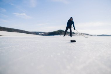 Yaşlı bir adam buz tutmuş bir gölde hokey sopasıyla diski sıkıştırma alıştırması yapıyor..