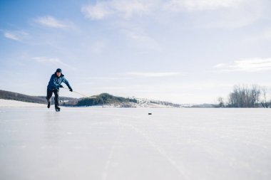 Yaşlı bir adam buz tutmuş bir gölde hokey sopasıyla diski sıkıştırma alıştırması yapıyor..