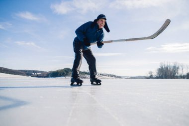 Yaşlı bir adam buz tutmuş bir gölde hokey sopasıyla diski sıkıştırma alıştırması yapıyor..