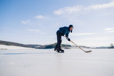 Yaşlı bir adam buz tutmuş bir gölde hokey sopasıyla diski sıkıştırma alıştırması yapıyor..