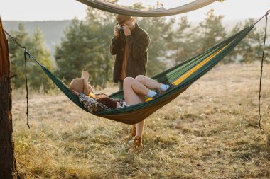 Çiftler dışarıda hamaklarda dinlenirken eğleniyorlar. Bir adam kamerada bir kızın fotoğrafını çekiyor..