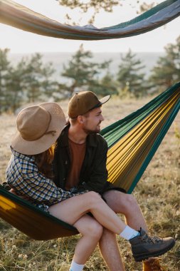 Birbirine aşık bir çift, doğada bir hamakta yatarken birbirlerine sarılıyorlar..
