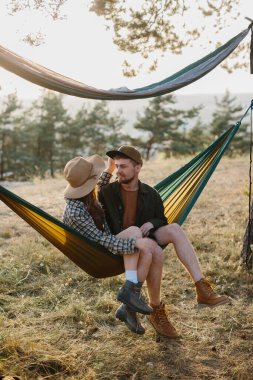 Birbirine aşık bir çift, doğada bir hamakta yatarken birbirlerine sarılıyorlar..