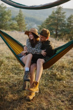 Birbirine aşık bir çift, doğada bir hamakta yatarken birbirlerine sarılıyorlar..