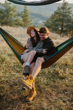 Birbirine aşık bir çift, doğada bir hamakta yatarken birbirlerine sarılıyorlar..