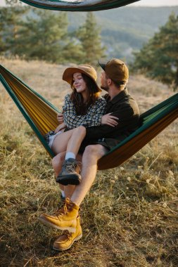 Birbirine aşık bir çift, doğada bir hamakta yatarken birbirlerine sarılıyorlar..