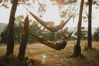 Bir erkek ve bir kız gün batımında bir çam ormanında hamaklarda dinleniyorlar. Dağlarda yürüyüş yaptıktan sonra hamaklarda dinlenen bir çift, ukulele çalan bir adam..