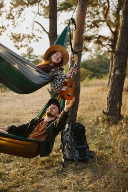 Bir erkek ve bir kız gün batımında bir çam ormanında hamaklarda dinleniyorlar.. 