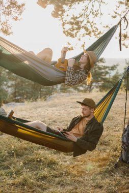 Bir erkek ve bir kız gün batımında bir çam ormanında hamaklarda dinleniyorlar.. 