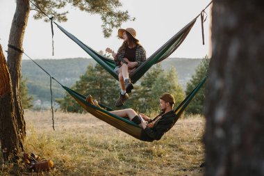 Genç bir adam ve güzel genç bir kadın dağlarda hamaklarda dinleniyorlar. Rahatlama ve doğayla bütünleşme kavramı..