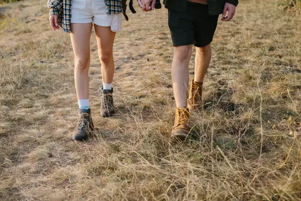 Bir adam ve bir kız dağlarda yürüyüş yaparken el ele tutuşuyorlar. Bacaklar yakın plan..