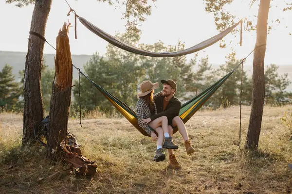 A couple in love relaxes in a hammock at sunset in a pine forest.