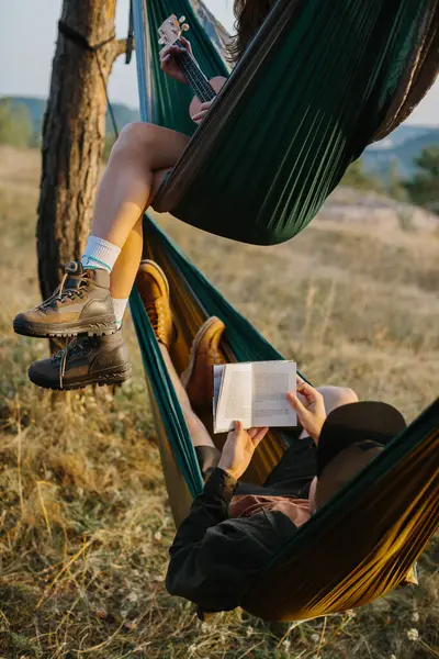 Aesthetic rest. A beautiful young girl and her boyfriend are relaxing in hammocks at sunset. Young people read and play musical instruments.