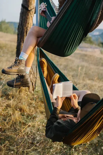 Aesthetic rest. A beautiful young girl and her boyfriend are relaxing in hammocks at sunset. Young people read and play musical instruments.