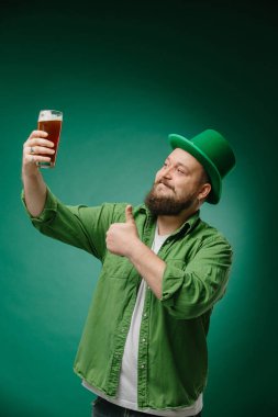 Koyu yeşil arka planda bira içen sakallı duygusal bir adam. Aziz Patrick Günü pankartı