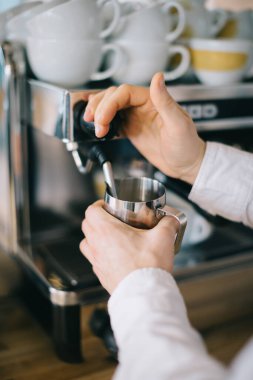 Bir barista espresso makinesi kullanarak kapuçino için süt hazırlar. Kafede kahve hazırlayan bir adamın yakın çekimi..