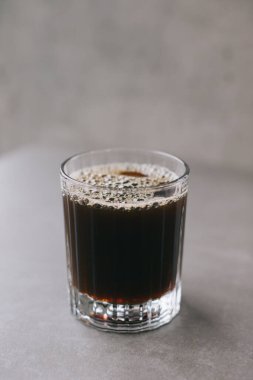 Cam bardakta taze demlenmiş damlatılmış kahve. Gri arka planda bir fincan kahve..