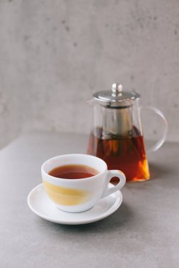 Gri arka planda izole edilmiş aromalı çay ile cam çaydanlık ve fincan..