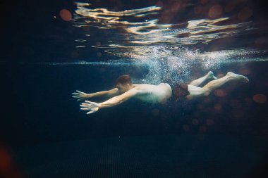 Genç bir adam bir havuzda su altında yüzer. Yaz tatili kavramı.
