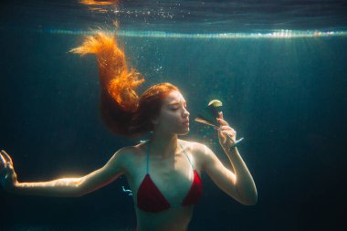 Güzel kızıl saçlı kadın yüzme havuzunda bir kokteyl ile poz veriyor. Yaz tatili kavramı.