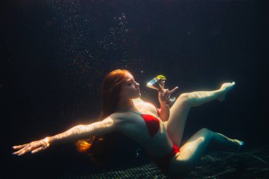 Güzel kızıl saçlı kadın yüzme havuzunda bir kokteyl ile poz veriyor. Yaz tatili kavramı.