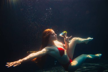 Güzel kızıl saçlı kadın yüzme havuzunda bir kokteyl ile poz veriyor. Yaz tatili kavramı.