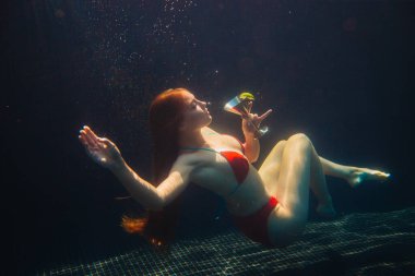 Güzel kızıl saçlı kadın yüzme havuzunda bir kokteyl ile poz veriyor. Yaz tatili kavramı.