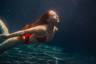 Genç kızıl saçlı kadın kaka içinde suyun altında yüzüyor.