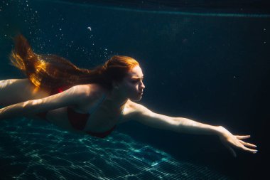 Genç kızıl saçlı kadın kaka içinde suyun altında yüzüyor.