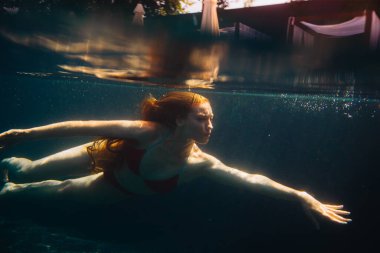 Genç kızıl saçlı kadın kaka içinde suyun altında yüzüyor.