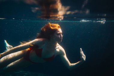 Genç kızıl saçlı kadın kaka içinde suyun altında yüzüyor.
