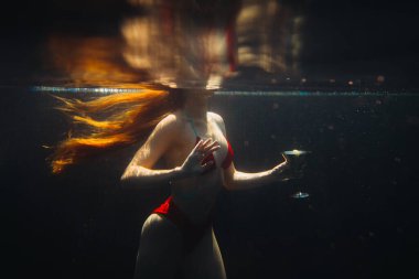 Güzel kızıl saçlı bir kadın suyun altında bir kokteyl ile poz veriyor..