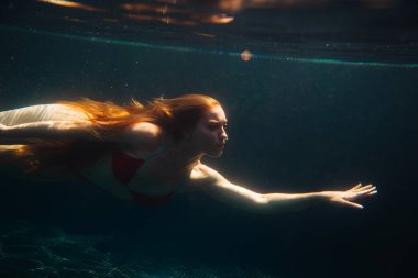 Genç kızıl saçlı kadın kaka içinde suyun altında yüzüyor.