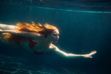 Genç kızıl saçlı kadın kaka içinde suyun altında yüzüyor.